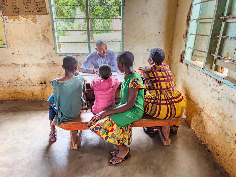 A Damico Health physician talks with a mother and her children across a wooden desk in a village clinic room.